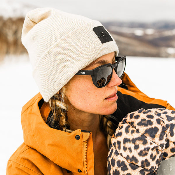 Woman in snow wearing a beanie and a leopard print glove and black sunglasses